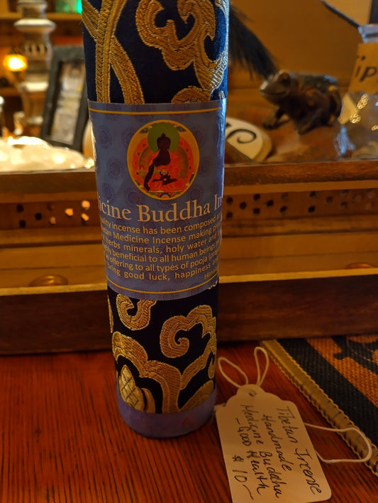 A silk-wrapped container of sapphire blue color with a re-closable lid, labeled as 'Medicine Buddha Incense' and containing 27 sticks for burning with decorative patterns in gold. Sold by Townsend Draft Goods